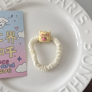 Détail d'un chouchou blanc avec un ours jaune tenant une fraise dans un plat blanc