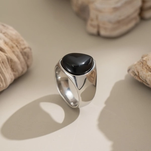 Détail d'une bague coeur en argent avec pierre noire sur une surface beige épurée