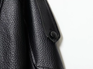 Macro-opname van zwart kunstleren jasje met litchi-textuur en beklede knopen detail