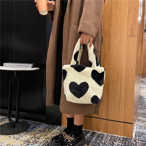 Chic white plush bucket bag with black heart pattern held by a model in a cozy setting