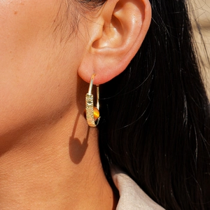 Detailed view of golden hoop earring with woven texture and a warm amber bead accent