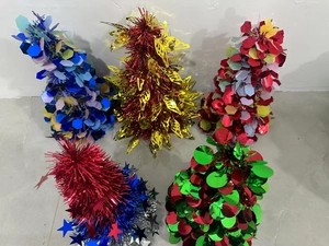 Top view of five colorful tinsel tabletop trees with stars and sequins on grey surface