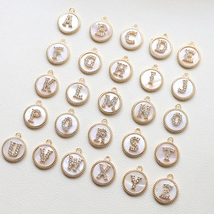 Macro detail of 26 gold-plated letter charms with zircon inlay and mother-of-pearl base