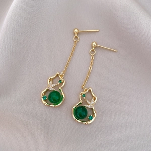 Close-up of golden gourd earrings with green stone and bamboo texture details