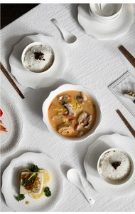 Flat lay of white embossed ceramic tableware set with elegant patterns on a textured tablecloth