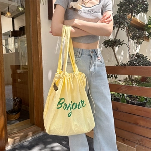 Detail of light yellow drawstring tote bag with green Bonjour text in French style
