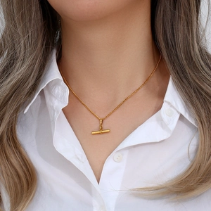 Close-up of a minimalist golden T-bar pendant necklace worn by a model on white shirt