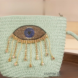 Detail showing mint green woven straw bag with rhinestone evil eye and tassel fringe