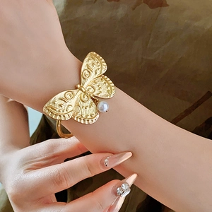 Close-up of vintage golden butterfly open cuff bracelet with an elegant pearl drop charm