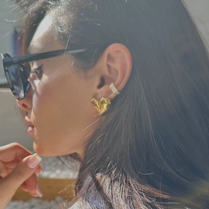 Close-up of heart-shaped gold stud earring and silver zircon ear cuff on ear