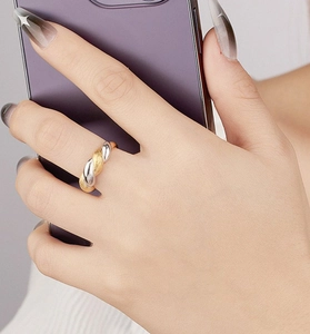 Detail of twisted silver and gold ring on hand holding a mobile phone in soft light