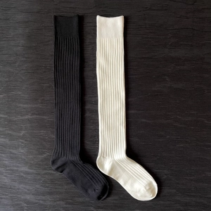 Detail of ribbed knit texture on black and cream over-the-knee socks laid on wood