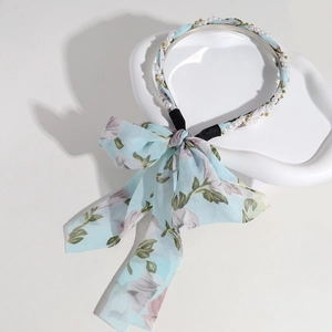 Detail of light blue floral bow headband with pearls and gold beads on white pedestal