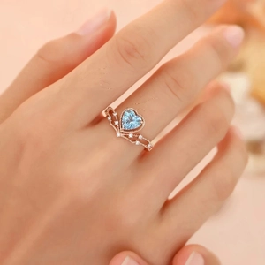 Rose gold heart-shaped blue topaz ring with crown design worn on model's hand