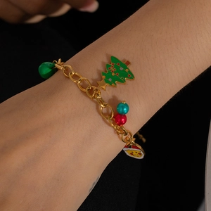 Close-up of golden Christmas charm bracelet with green tree and red beads on wrist