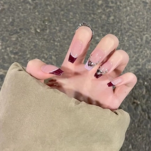 Detail of coffin shape press-on nails with red French tips and heart rhinestone accents