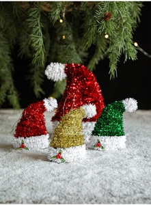Close-up of sparkling sequin mini Christmas hats with plush trim on snowy pine background