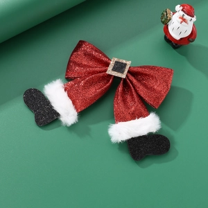 Detail of Christmas bow hair clip with red sequins and Santa boots on green background