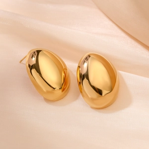 Minimalist gold lip-shaped stud earrings on beige silk fabric with reflective finish