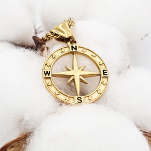 Detail of gold-plated stainless steel compass pendant with a star on white cotton