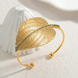 Golden open cuff bracelet featuring hollow leaf design with green zircon accents