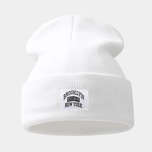 Close-up of white knit beanie featuring a stitched Brooklyn patch with fine ribbed texture