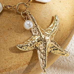 Macro shot of gold starfish pendant with pearl and shell inlay detail on a golden chain