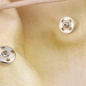 Macro de boutons pression en métal argenté sur un tissu jaune pâle à texture fine