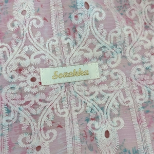 Detailed close-up of pink lace fabric with white embroidery and Sozakka gold woven label