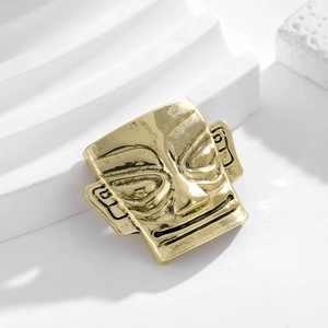 Detailed close-up of a golden metal Sanxingdui mask brooch against white props