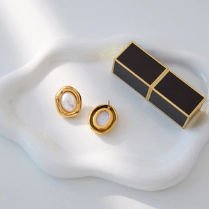 Macro shot of oval 18K gold plated stainless steel resin pearl earrings on white tray