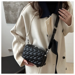 Detail of black quilted crossbody bag with adjustable wide strap and mini pouch charm