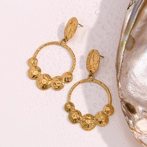Detailed view of gold hammered disc earrings next to a shell with water droplets