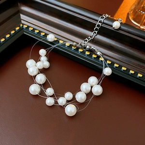 Detail view of a multi-layer faux pearl bracelet with silver clasp on brown leather