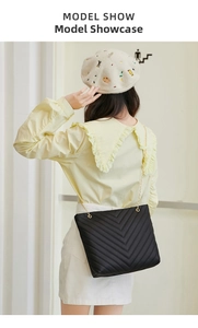 Detail of black V-quilted faux leather shoulder bag with gold chain strap on model
