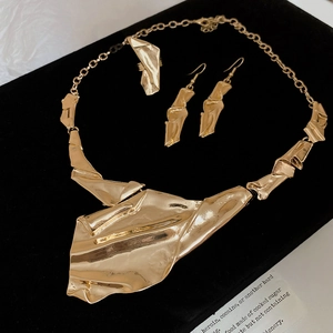Detail of gold irregular pleated jewelry set with necklace and earrings on a black stand