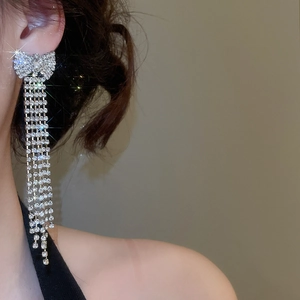 Detail of silver bow tassel earrings with sparkling rhinestones worn on the ear