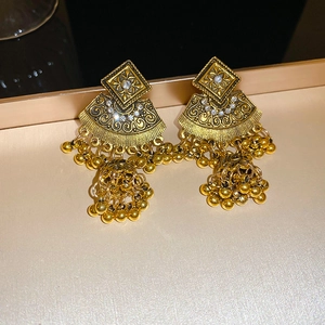 Detailed macro view of vintage ethnic golden Jhumka earrings with tassels and white rhinestones