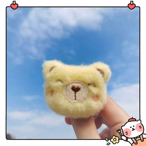 Close-up of yellow plush bear brooch with embroidered details held against a blue sky
