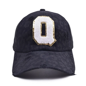 Close-up of distressed black mesh baseball cap with sequined letter Q patch embroidery