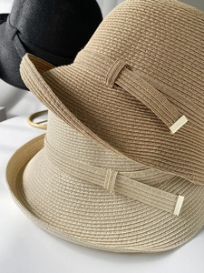 Dettaglio di cappelli in paglia intrecciata in nero, kaki e beige con fibbie dorate