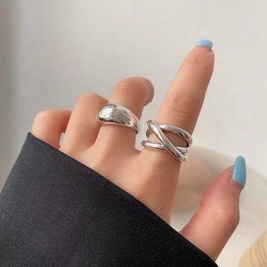 Close-up of minimalist silver wide band and triple layered crossover rings on finger