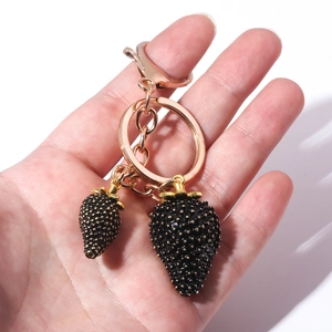 Close-up of black strawberry keychain with gold seeds and clasp held in hand