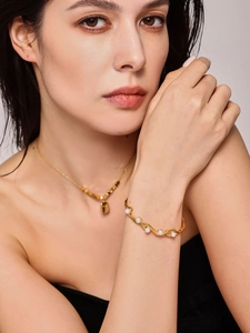 Detail shot of wavy gold open cuff bracelet with pearls and matching rectangle tag necklace