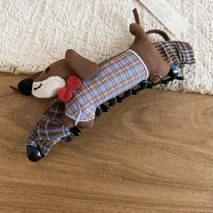 Detail view of a dachshund plush hair clip with blue plaid coat and red bowtie