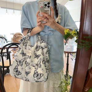 Detail of white suede tote bag featuring black butterfly print and woven handles