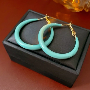 Boucles d'oreilles créoles rondes vert sarcelle sur une boîte à bijoux noire et fond rouge