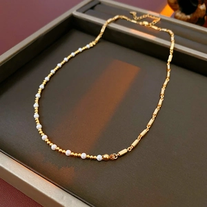 Detail view of gold beaded pearl necklace with cylinder tube links on jewelry tray