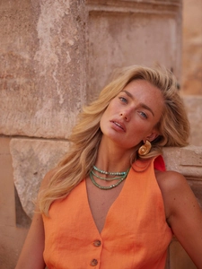 Close-up of golden spiral shell earrings and turquoise beaded layered necklace on model