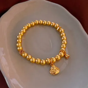Oriental zen matte gold bead bracelet with buddha and lotus pod charms on white plate